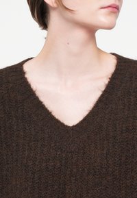 Smeđa pletena majica s V-izrezom i rebrastom teksturom, od mekanog, laganog materijala s blago dlakavom završnom obradom.