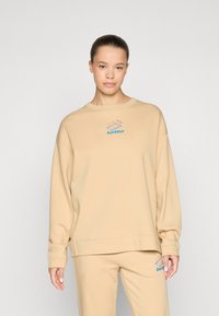 Beige sweatshirt with a round neckline and dropped shoulders, featuring a small blue and orange Lotto logo on the chest. Soft, textured fabric.
