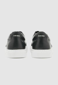 Schwarze Ledersneaker mit weißen Akzenten, ausgestattet mit einer glatten Textur und einer flachen Gummisohle. Der Markenname "REISS" ist auf der Ferse geprägt.