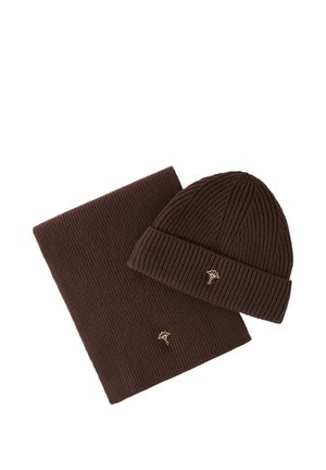 Cappello a coste marrone e set di sciarpa abbinata, ciascuno con un piccolo emblema a foglia dorata ricamato su un lato.
