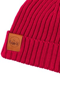 Jasnoczerwona prążkowana dzianinowa czapka z podwiniętym brzegiem i brązową skórzaną naszywką z motywem gór, drzew i niedźwiedzia.