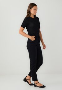 Czarna dopasowana bluzka z krótkim rękawem, zestawiona z taliowanymi czarnymi spodniami i płaskimi czarnymi butami. Gładka tekstura materiału i smukła sylwetka.