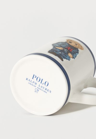 Λευκή πορσελάνινη κούπα με μπλε ναυτικό χείλος και λαβή, με αρκούδα ντυμένη με τζιν και το λογότυπο "Polo Ralph Lauren" στη βάση.