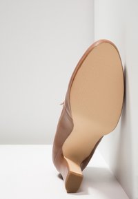 Chaussure de ville pour femmes en cuir marron avec petit talon carré, vue de la semelle de face sur fond d'angle blanc.