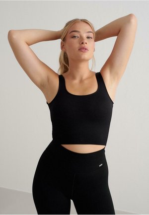 Black ribbed crop top with wide straps and a fitted design, paired with high-waisted black leggings featuring a cut-out detail.
