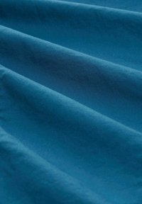 Türkisfarbener Stoff mit glatter Textur, der dezente Falten aufweist, die Tiefe und Dimension schaffen. Die Oberfläche wirkt weich und gleichmäßig.