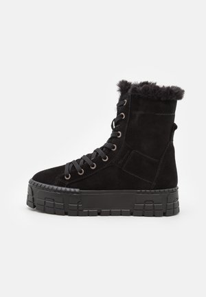 Mustat mokkanahka ankle boots, joissa on karvainen vuori, pyöreä kärki ja erottuva paksu kumipohja geometrisilla kuvioilla ja metallisilla silmukoilla.