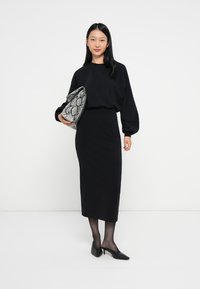 Čierny dlhý rukáv top a priliehavá midi sukňa nosená s čiernymi mule topánkami. Model drží sivú kabelku s hadou textúrou. Jednoduchý, elegantný dizajn.