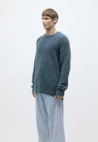 Light blue oversized sweater with a textured pattern, long sleeves, and ribbed cuffs, paired with wide light denim pants.
