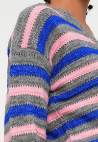 Stripet genser i grått, rosa og blått garn. Har striper i varierende bredder med en myk tekstur og v-hals.