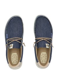 Lässige Denim-Schuhe mit einem navyblauen Obermaterial, hellbraunen Schnürsenkeln und einer strukturierten Sohle. Verfügt über ein Etikett an der Zunge mit "HEY DUDE" Branding.