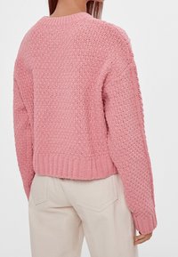 Suéter de punto rosa con un corte holgado, diseño texturizado y dobladillo acanalado. Presenta mangas largas y un cuello redondo.