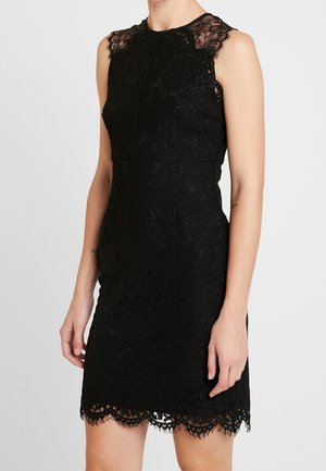 Mouwloze zwarte kanten jurk met een geschulpte zoom, gedragen door een persoon tegen een effen lichte achtergrond, waarbij de romp en bovenbenen zichtbaar zijn.