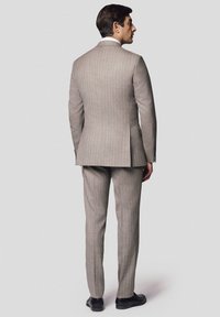 Szary garnitur w prążki o dopasowanym kroju. Materiał wydaje się gładki, a marynarka ma jeden rozcięcie i klapy w kształcie litery "notch". Nosi czarne buty.