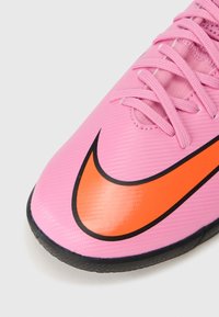 Rosa syntetisk fotballsko med svart og oransje Nike-svikt, med teksturert overdel, rund tå og snøring.