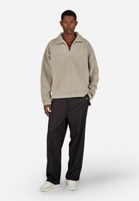 Világosszürke, galléros boleró, laza szabással. Fekete nadrággal és fehér sportcipővel párosítva.