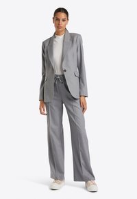 Grauer maßgeschneiderter Blazer mit Reverskragen und einem Knopf, kombiniert mit grauen weiten Hose mit elastischem Kordelzugbund.
