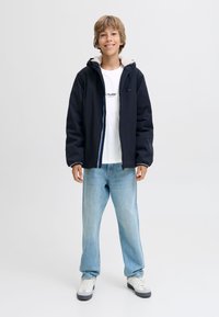 Must kapuutsiga jope valge fliisis voodriga, kantud üle valge t-särgi ja hele siniste teksade. Hallid tossud valgete detailidega.