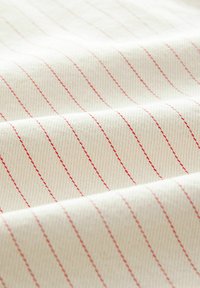 Katoenen stof met een crèmekleurige basis en fijne rode verticale strepen, met een gladde textuur en een licht ribbelige weefsel.