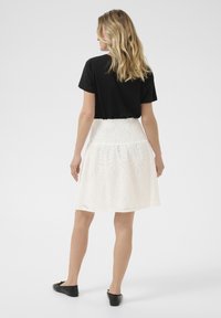 Jupe blanche brodée avec un taille smockée, ornée de motifs floraux découpés. Associée à un haut noir à manches courtes et des ballerines noires.