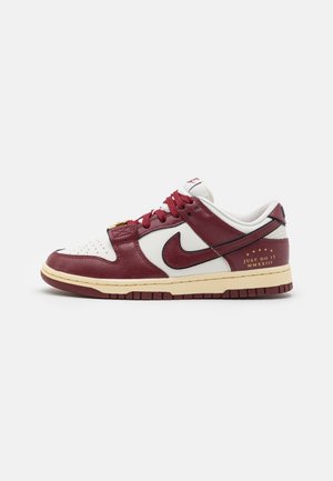 Niskie sneakersy w białym i ciemnoczerwonym kolorze z logo Nike, bordowymi sznurowadłami i złotym napisem "Just Do It MMXXIII" na pięcie.