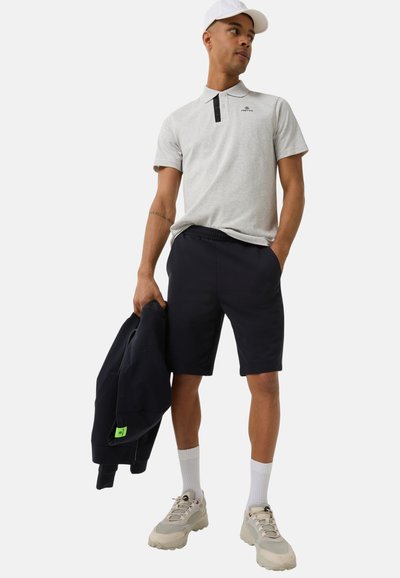 Hellgraues Polohemd mit schwarzem Kragen, marineblaue Shorts und cremefarbene Sneakers. Zubehör umfasst einen dunklen Sweatshirt und eine weiße Mütze.