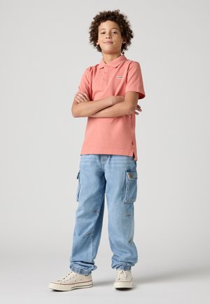Polo rose avec un petit logo, associé à un pantalon cargo bleu clair avec des poches latérales et des poignets élastiques, complété par des baskets blanches.