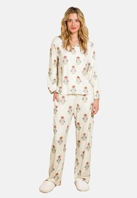 Crème kleurige pyjama met een bloemenpatroon in rood en blauw; lange mouwen top met kraag en broek met elastische taille. Gecombineerd met pluizige slippers.