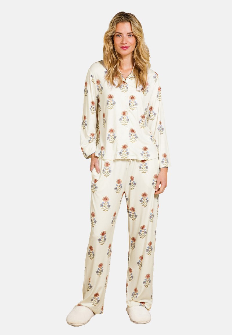 Crème kleurige pyjama met een bloemenpatroon in rood en blauw; lange mouwen top met kraag en broek met elastische taille. Gecombineerd met pluizige slippers.