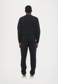 Marineblå sweatshirt med ribbede manchetter og kant, sammen med matchende marineblå bukser. Materialet ser blødt og tekstureret ud. Minimalistisk design.