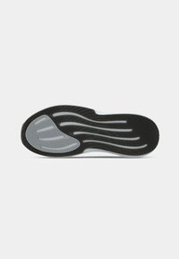 Σόλα παπουτσιού με μαύρο και γκρι ελαστικό πέλμα που διαθέτει κυματιστές και καμπυλωτές αυλακώσεις για πρόσφυση σε επίπεδη λευκή επιφάνεια.