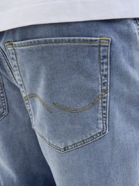 Light blue denim jeans feature a back pocket with yellow stitching and a curved design. The texture appears smooth and slightly faded.