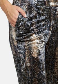 Pantaloni con motivo di pelle di serpente in morbido velluto, caratterizzati da tonalità di marrone, grigio e nero. Include una tasca laterale per una maggiore funzionalità.
