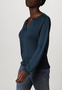 Türkise Bluse mit langen Ärmeln und Kragen mit Knopfverschluss, aus weichem Stoff und mit lockerer Passform. Verfügt über Knopfakzente und elastische Bündchen.