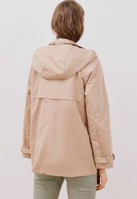 Beige, huva jacka med avslappnad passform, med baköppning och justerbara ärmmuddar, tillverkad av ett mjukt, vattenavvisande material.