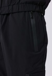 Pantaloni neri con vita elastica e una tasca con zip verticale impermeabile sul lato.