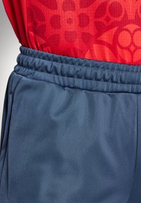 Rode mouwloze shirt met een gestructureerd bloemenpatroon, gecombineerd met blauwe sportshorts met een elastische tailleband en een gladde stof.
