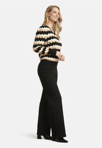 Black and cream zigzag patterned sweater with a v-neck and fitted cuffs, paired with black wide-legged pants and black heeled shoes.