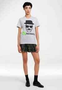 Gray cotton t-shirt with a black graphic and green "Heisenberg" text. Paired with a green plaid flared skirt and black shoes.