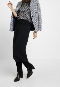 Cappotto a motivo houndstooth bianco e nero sopra un maglione nero e culotte nere, abbinato a stivali neri con tacco alti fino al ginocchio.