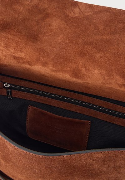 Intérieur de sac en daim marron avec doublure en tissu noir, une poche zippée et une étiquette de marque en daim attachée.