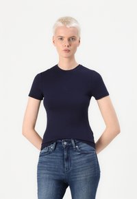 Mørkeblå kortermet t-skjorte i en tettsittende design med rund hals, laget av glatt stoff, kombinert med blå jeans.