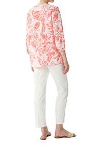 Rosa Bluse mit rotem Blättermuster, Dreiviertelärmel. Kombiniert mit weißen, schmal geschnittenen Hosen und hellbraunen Sandalen. Glattes, leichtes Material.
