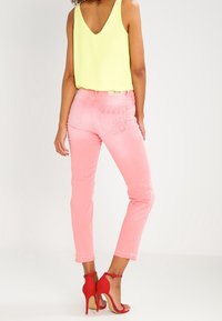 Jeans rosas de corte ajustado, combinados con una blusa sin mangas de un amarillo brillante. El conjunto incluye sandalias de tacón alto rojas y un diseño en la parte posterior de los jeans.