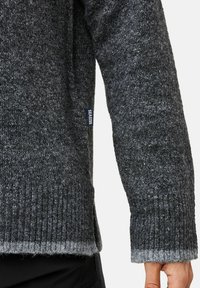 Maglione lavorato a maglia grigio scuro con orlo e polsini a coste. Presenta una sfumatura grigio chiaro nella parte inferiore e un piccolo tag blu "Seaside" sul lato.