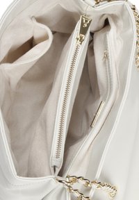 Biała syntetyczna torebka wnętrze z beżowym materiałem wykończeniowym, wieloma kieszeniami i złotym zamkiem błyskawicznym dla bezpiecznego zamknięcia.