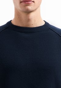 Marineblauwe gebreide trui met een textuurpatroon, geribbelde ronde hals en raglanmouwen, gekenmerkt door een soepele afwerking en subtiele details.