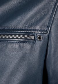 Marinelederstoff mit einer Nahaufnahme von einer Reißverschlusstasche mit Metallbeschlägen, strukturiertem Oberflächen und kontrastierender Nahtdetail.