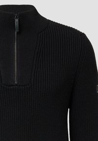 Czarny sweter robiony na drutach z wysokim kołnierzem, z pół zamek błyskawiczny. Materiał ma teksturowaną powierzchnię z prążkowanymi detalami.
