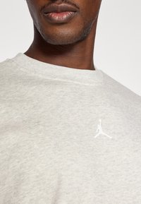 Felpa grigia in cotone con collo rotondo, caratterizzata da un logo Jumpman bianco sul petto. Texture liscia, design minimal.